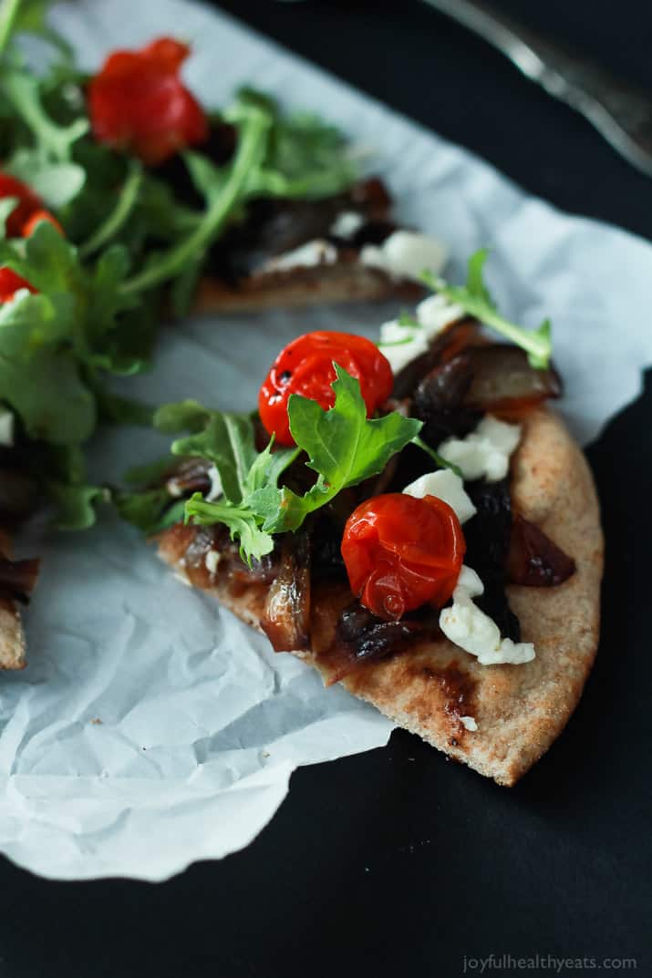 Close-up of a slice of Pita Pizza with balsamic caramelized onions, tomatoes, feta, and arugula
