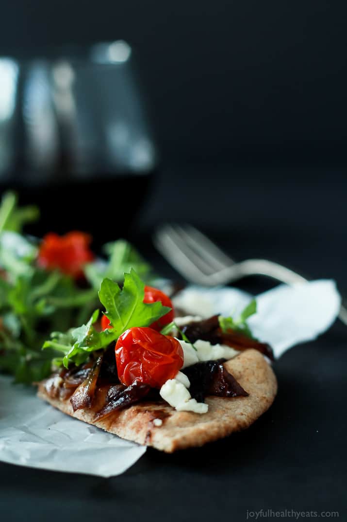 A slice of Pita Pizza with balsamic caramelized onions, feta, tomatoes, and arugula