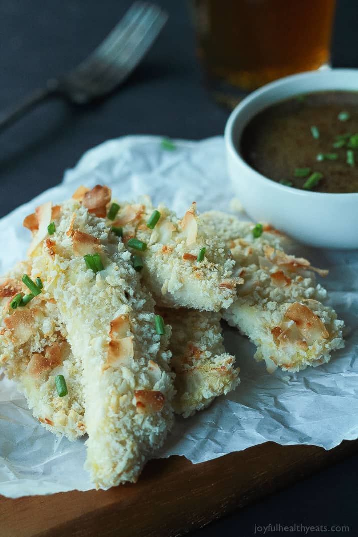 Coconut Crusted Chicken Tenders with a cup of Honey Mustard Sauce on parchment paper