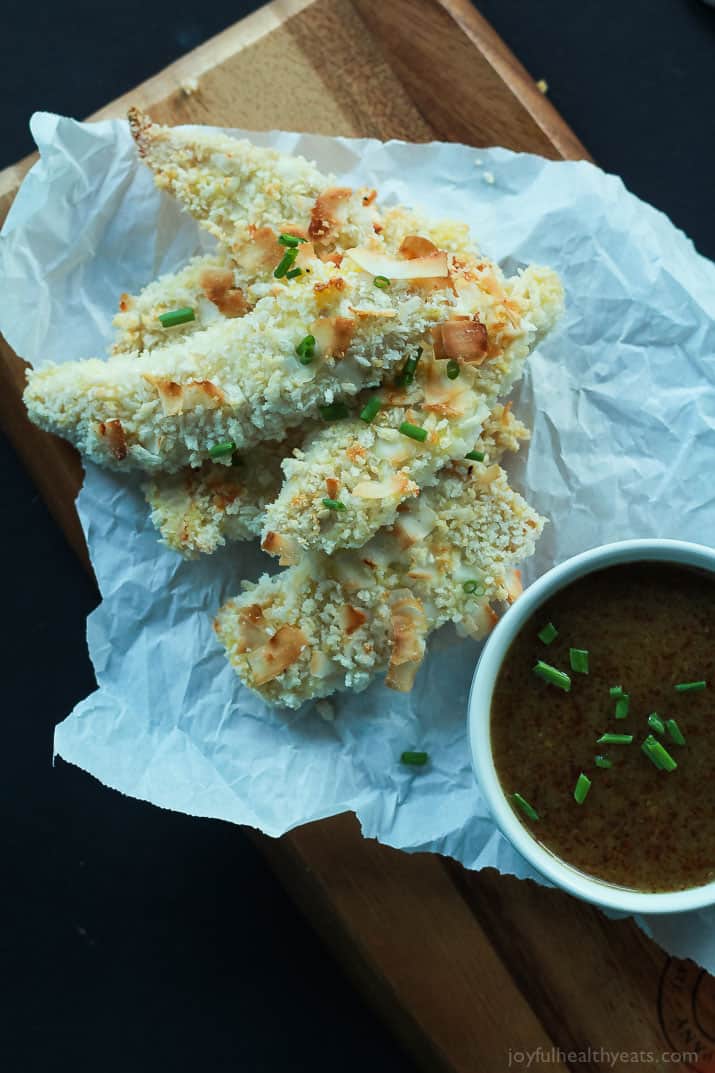 Top view of Coconut Crusted Chicken Tenders with a cup of Honey Mustard Sauce on parchment paper