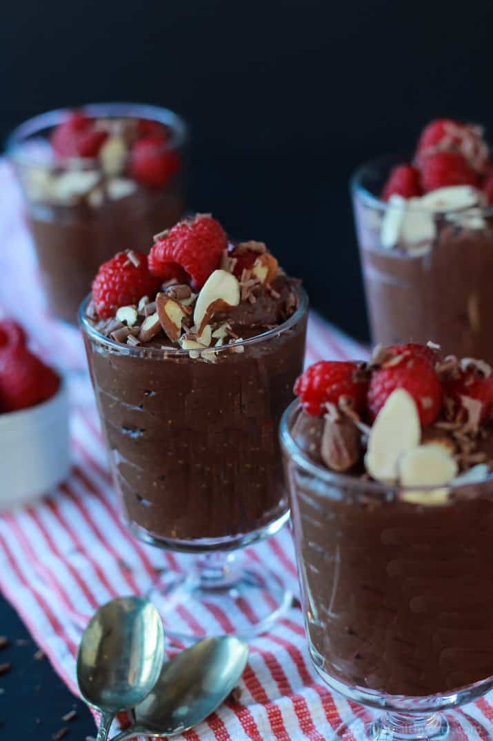 Dessert glasses of Chocolate Chia Pudding, topped with sliced almonds, shaved chocolate and fresh raspberries