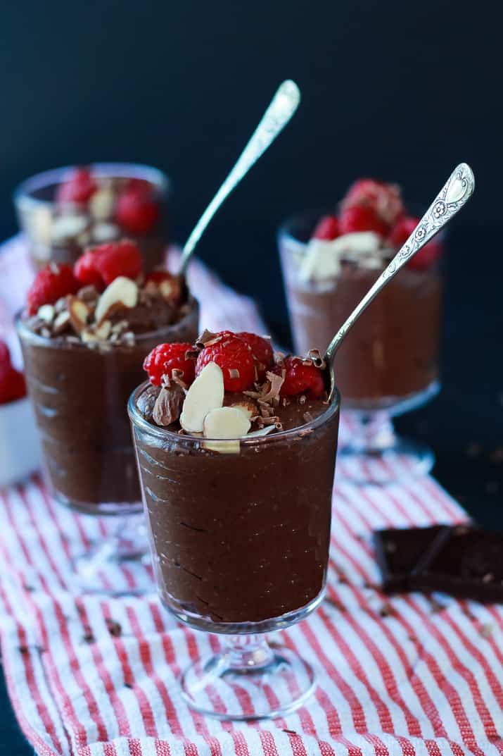 Dessert glasses of Chocolate Chia Pudding, topped with sliced almonds, shaved chocolate and fresh raspberries
