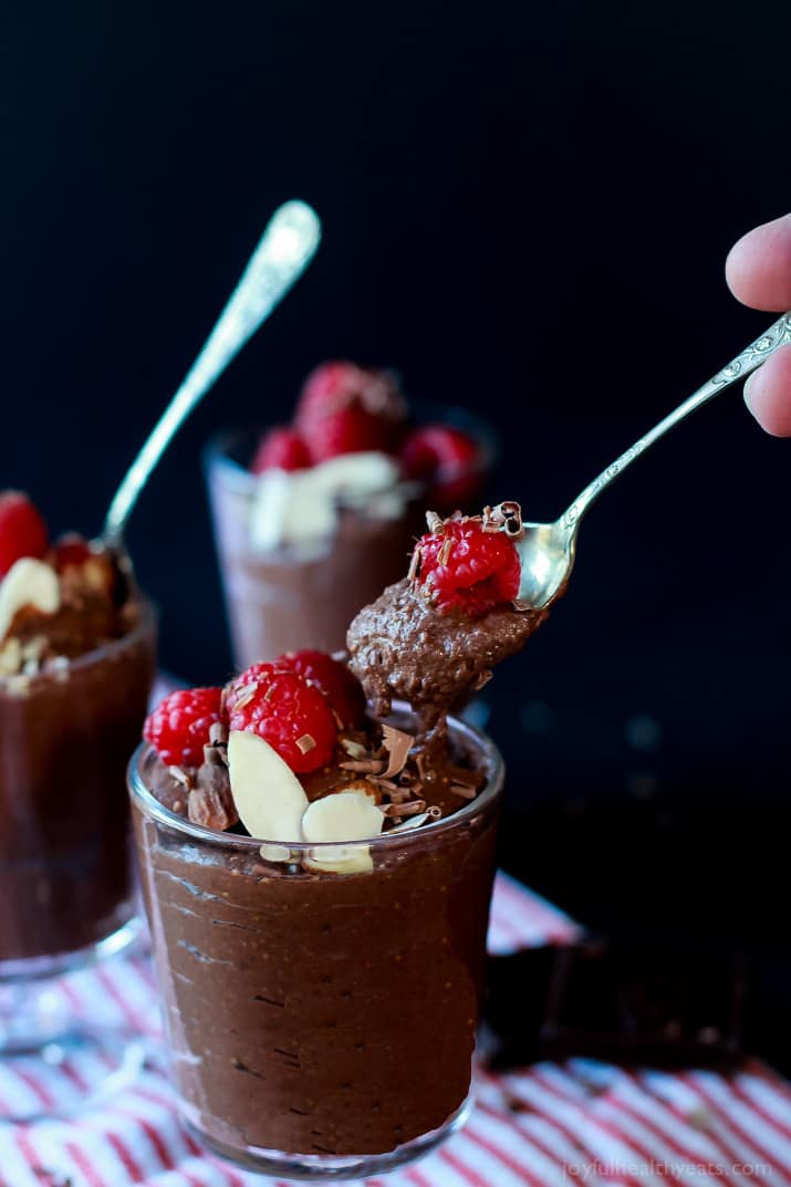 Dessert glasses with spoons of Chocolate Chia Pudding, topped with sliced almonds, shaved chocolate and fresh raspberries