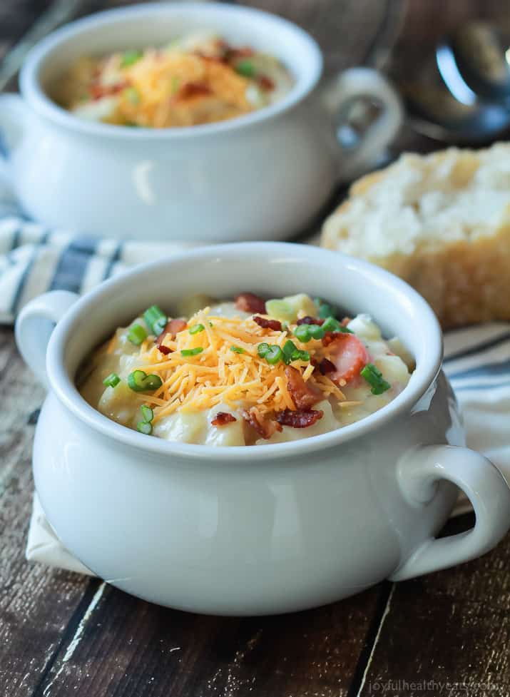 Two crocks of Creamy Potato Leek Soup topped with shredded cheese, scallions and bacon