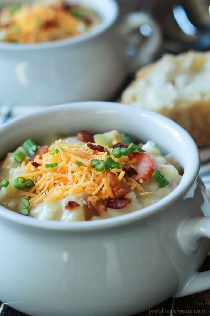 Close-up of Creamy Potato Leek Soup in a crock topped with shredded cheese, scallions and bacon