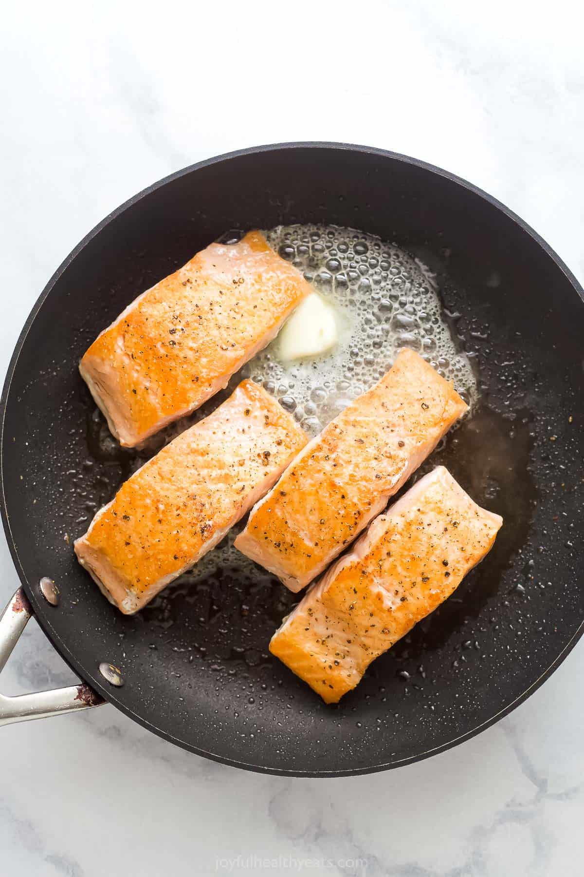 Flipping the salmon and adding the ،er to the pan.