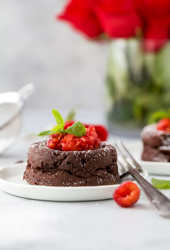 side photo of photo of nutella chocolate lava cake topped with champagne muddled raspberries on a plate with roses in background