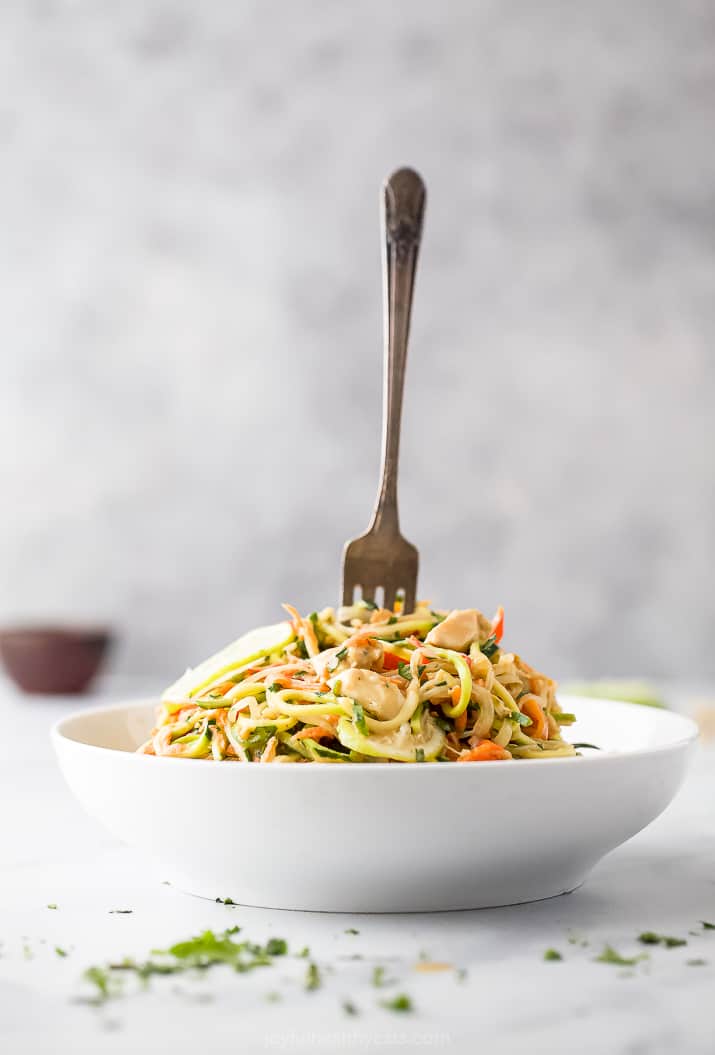 a bowl filled with thai chicken zucchini noodles and a fork in the bowl