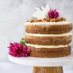 close up photo of The BEST Hummingbird Cake Recipe with Light Cream Cheese Frosting on a cake platter with flowers on top