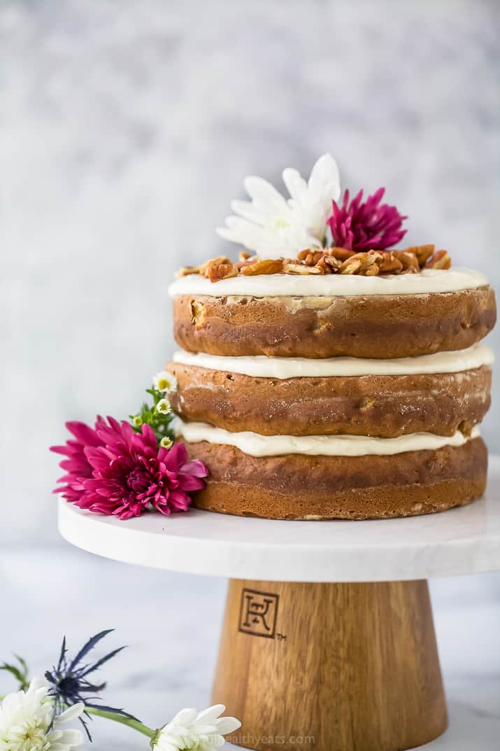 close up photo of The BEST Hummingbird Cake Recipe with Light Cream Cheese Frosting on a cake platter with flowers on top