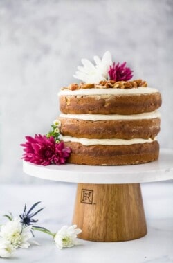 The BEST Hummingbird Cake Recipe with Light Cream Cheese Frosting on a cake platter with flowers