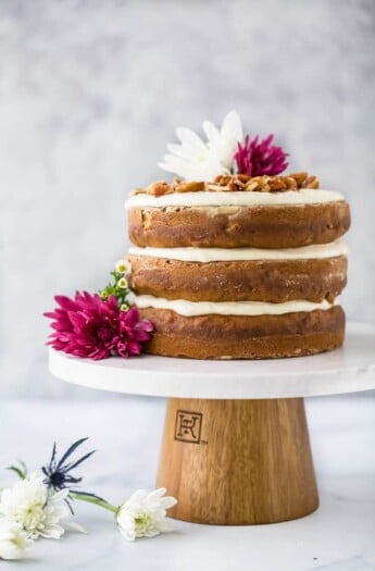 The BEST Hummingbird Cake Recipe with Light Cream Cheese Frosting on a cake platter with flowers