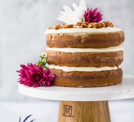 The BEST Hummingbird Cake Recipe with Light Cream Cheese Frosting on a cake platter with flowers