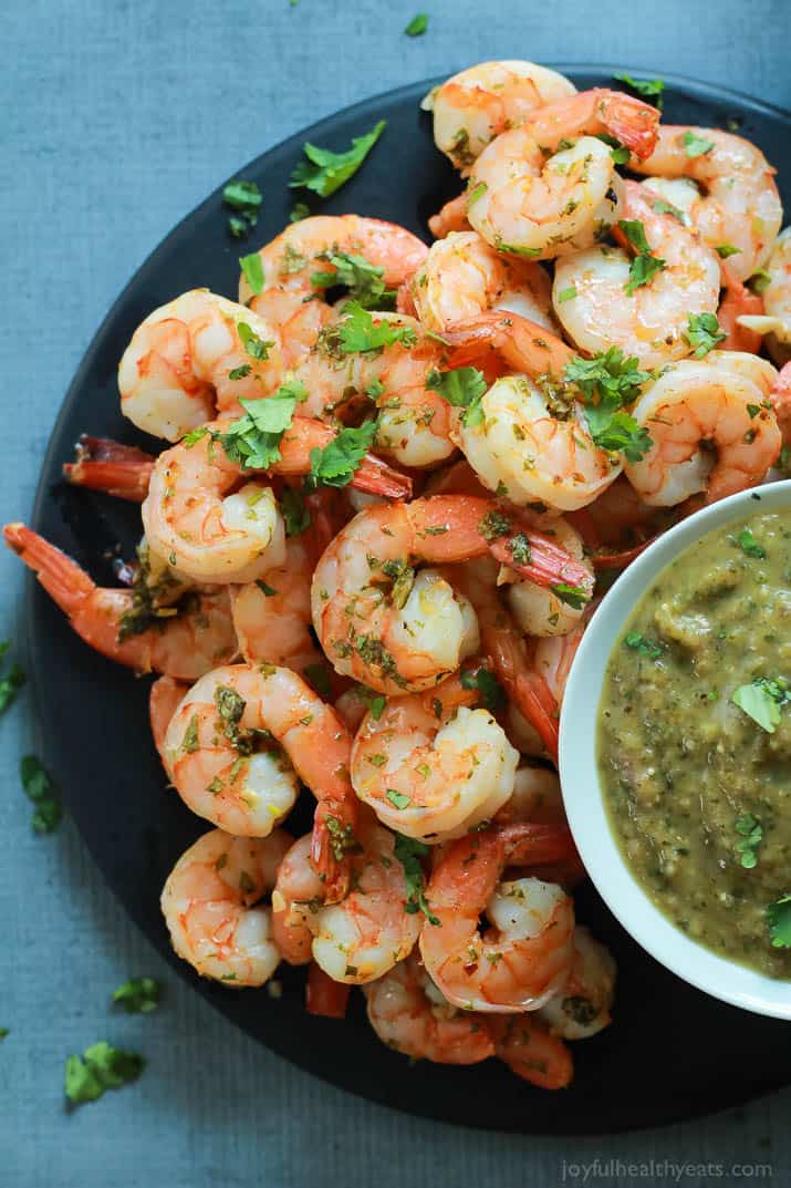 Top view of Cilantro Lime Roasted Shrimp on a plate with a cup of homemade Roasted Tomatillo Sauce