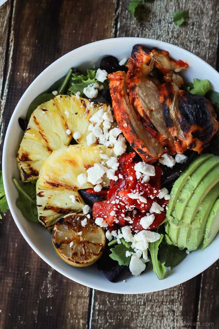 Top view of a bowl of Harissa Lime Grilled Chicken Salad with grilled pineapple, limes, and fresh avocado