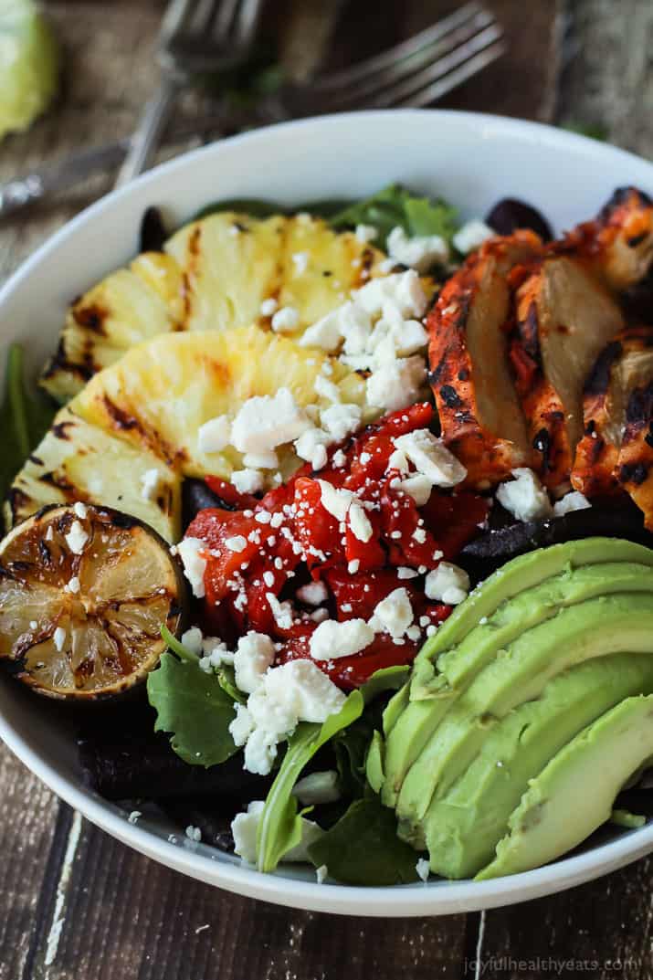 Harissa Lime Grilled Chicken Salad in a bowl with grilled pineapple, roasted red pepper, sliced avocado and crumbled feta