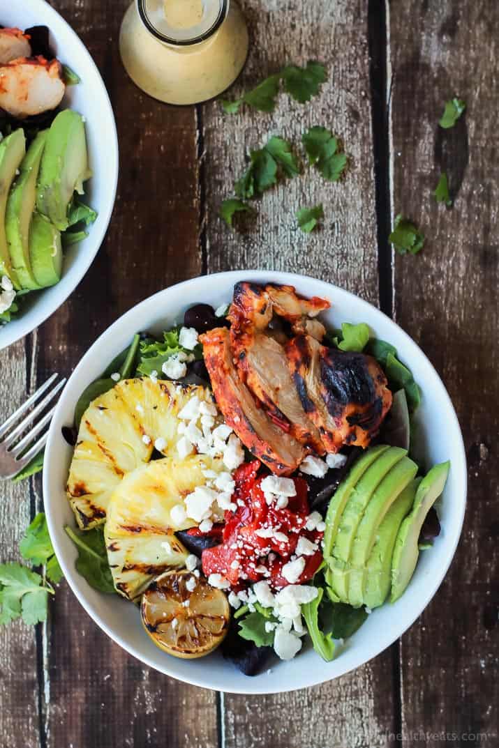 Top view of Harissa Lime Grilled Chicken Salad in a bowl with grilled pineapple, sliced avocado, roasted red pepper and crumbled feta