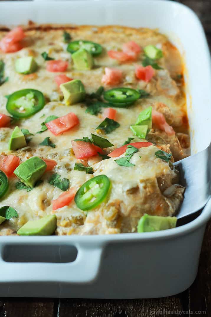 Close-up view of a pan of Chicken Enchiladas topped with melted cheese, jalapeno, avocado, and tomato