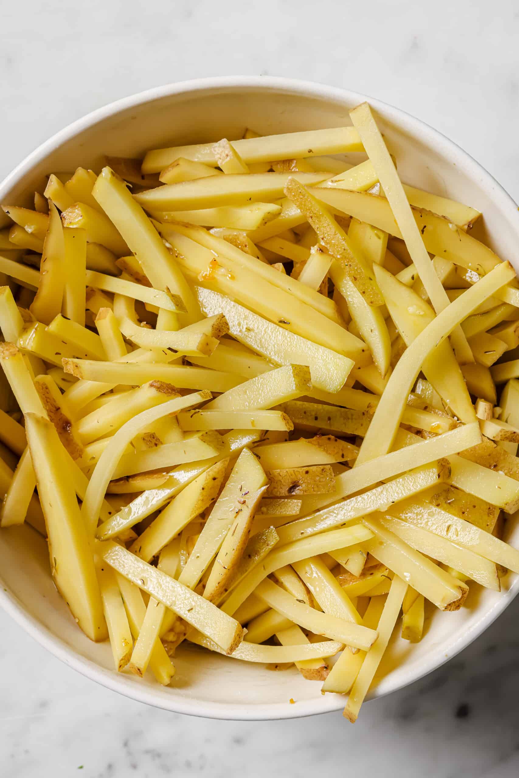 This baked garlic parmesan fries recipe is so good it might tempt you into eating the whole tray on your own. Good thing they're healthy! Tossing the potatoes with olive oil and garlic.
