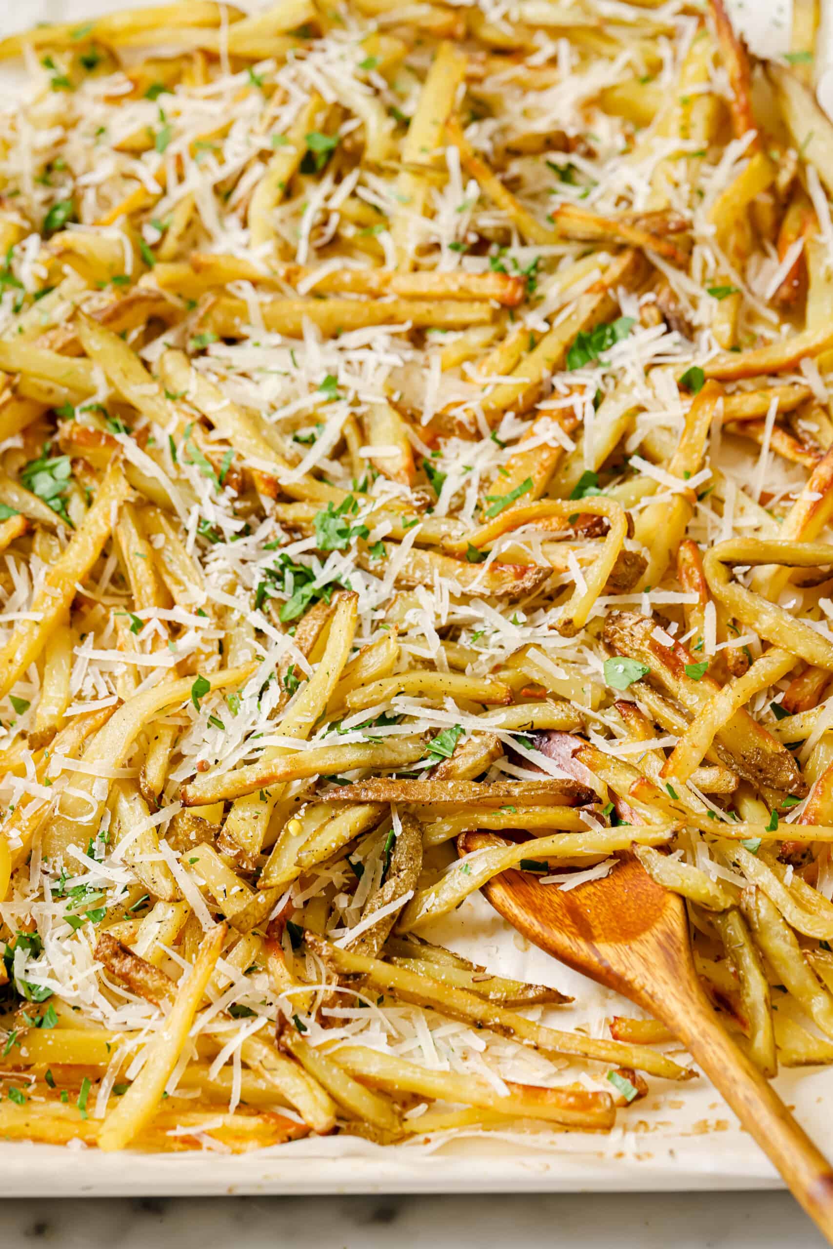 This baked garlic parmesan fries recipe is so good it might tempt you into eating the whole tray on your own. Good thing they're healthy! Close-up of crispy baked french fries.