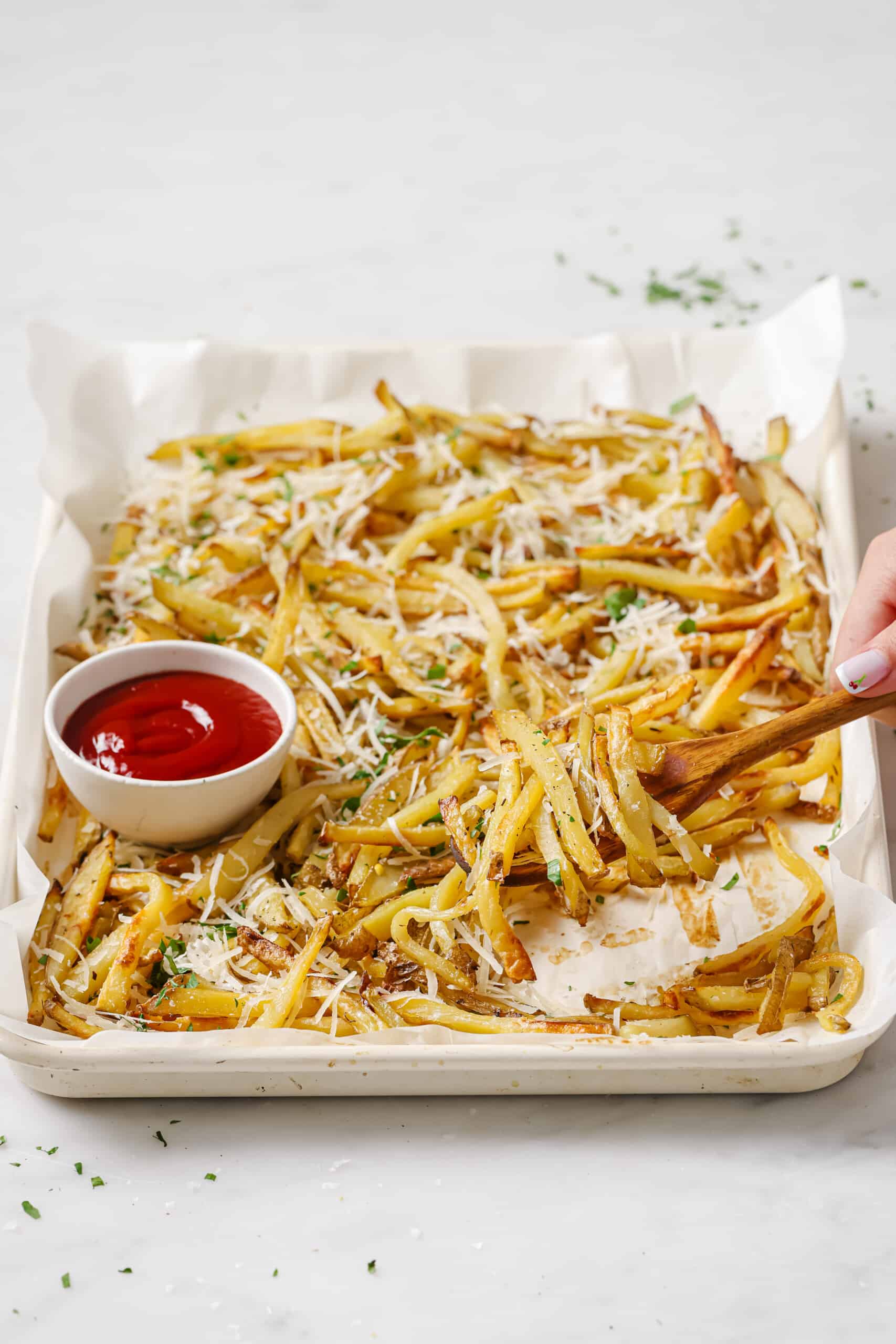 This baked garlic parmesan fries recipe is so good it might tempt you into eating the whole tray on your own. Good thing they're healthy! A tray of crispy fries with ketchup on the side.