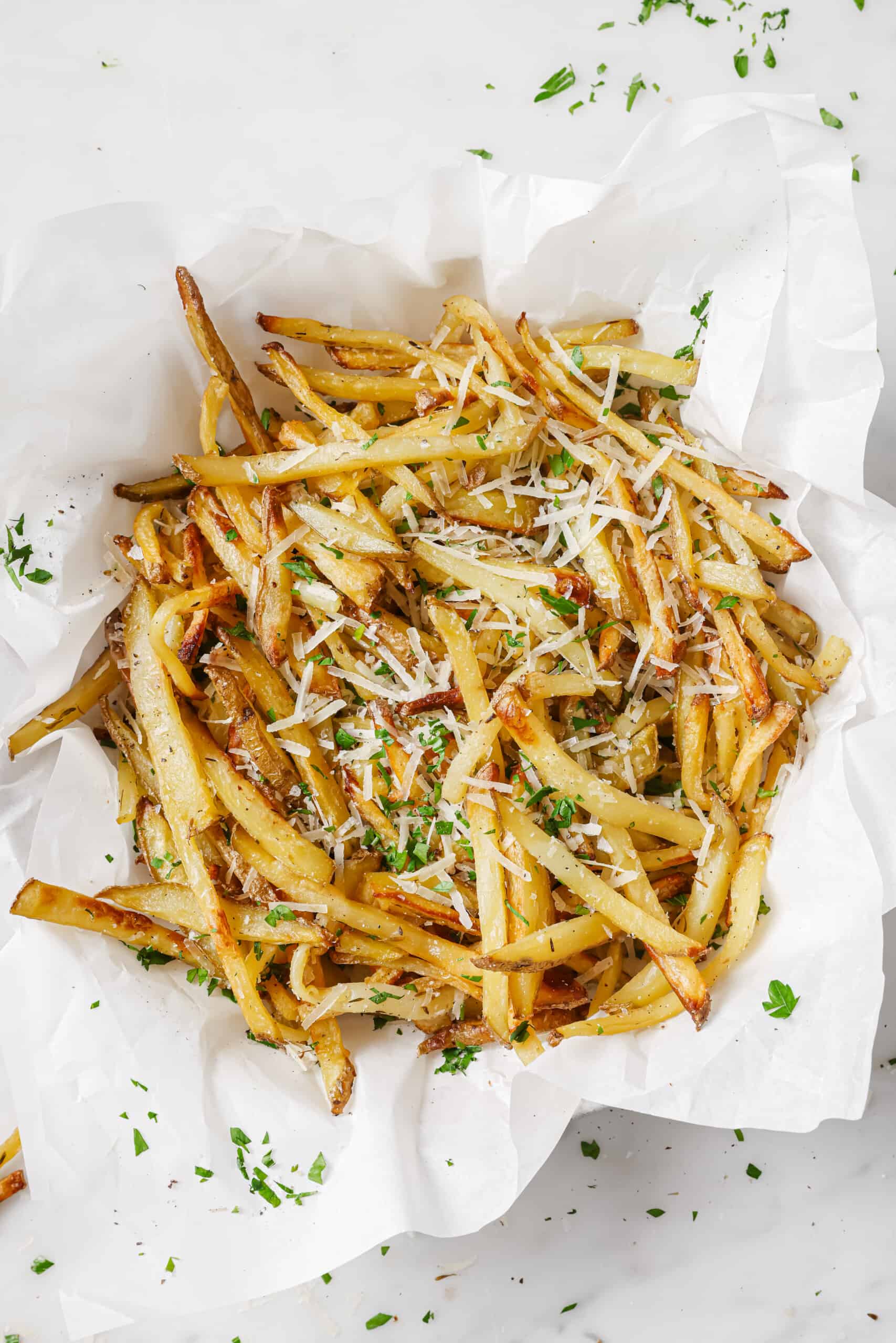 This baked garlic parmesan fries recipe is so good it might tempt you into eating the whole tray on your own. Good thing they're healthy! Lots of baked french fries with parmesan on top.