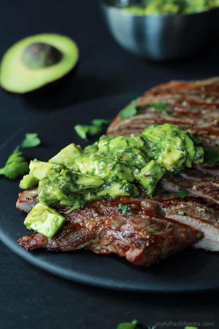 Grilled steak topped with fresh chimichurri sauce on a black plate 