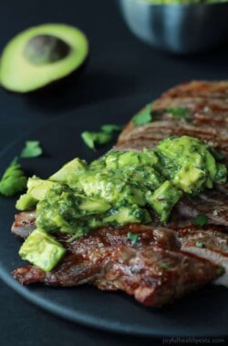 Close up of a Juicy Grilled Flank Steak topped with a fresh Avocado Chimichurri on a black plate
