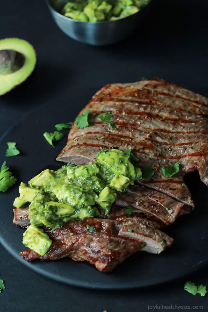 Sliced grilled Flank Steak with fresh Chimichurri sauce on a black plate 