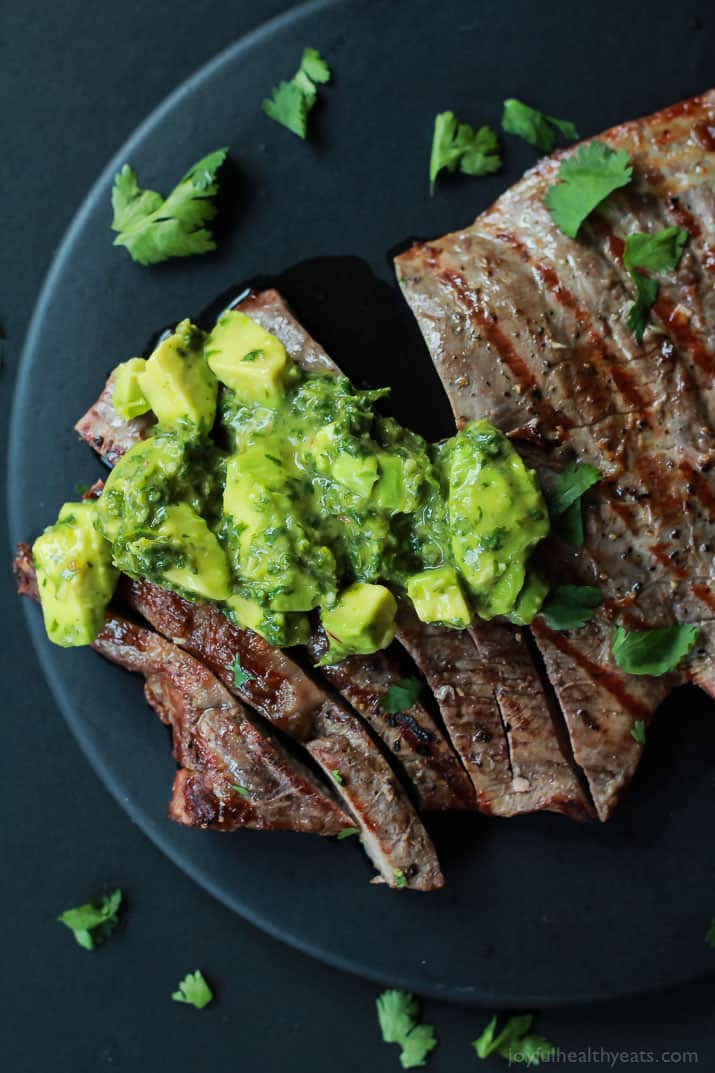 Top view of Grilled Flank Steak with Avocado Chimichurri on a black plate sprinkled with cilantro 