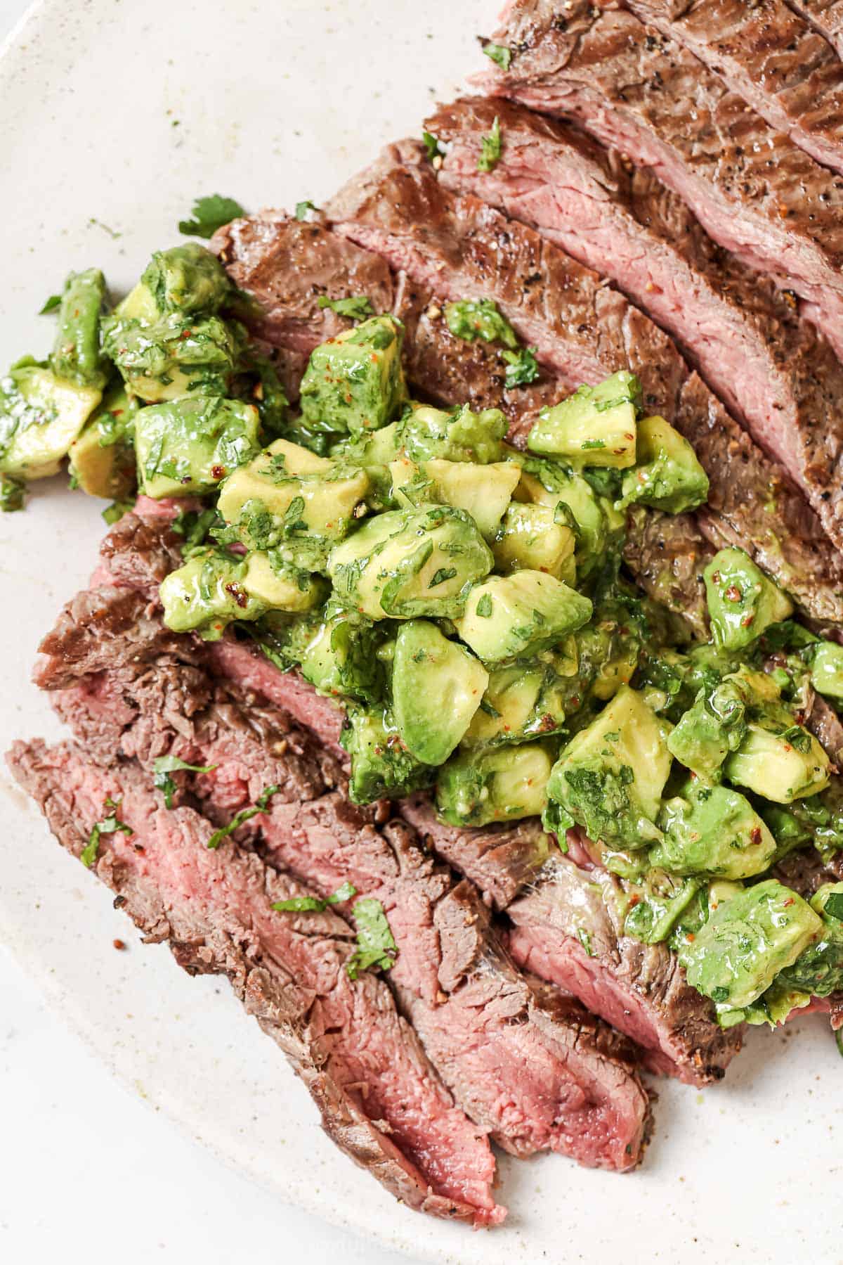 This juicy Grilled Flank Steak with Avocado Chimichurri is an easy recipe that’s full of flavor. It’s ready in less than 20 minutes! Overhead view of sliced grilled flank steak on plate with avocado chimichurri on top