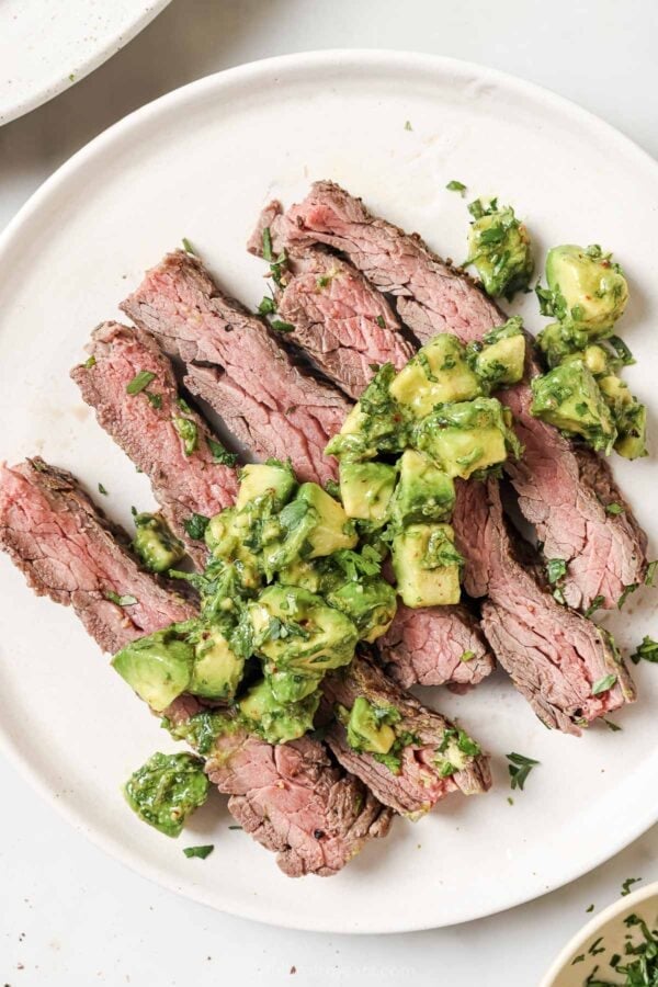 Overhead view of sliced grilled flank steak on plate with avocado chimichurri on top