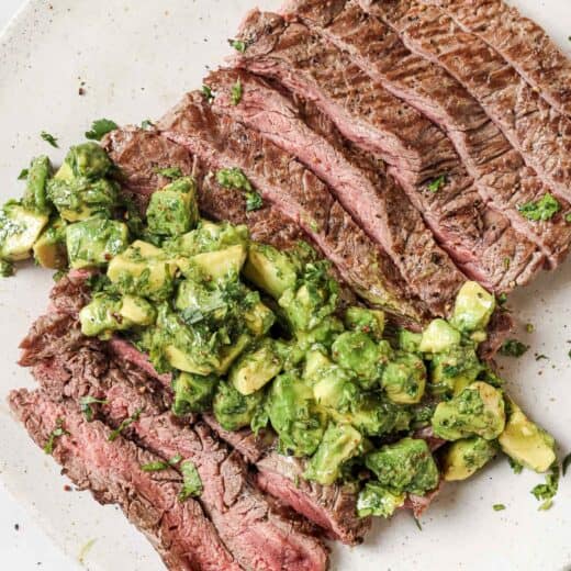 Overhead view of sliced grilled flank steak on plate with avocado chimichurri on top