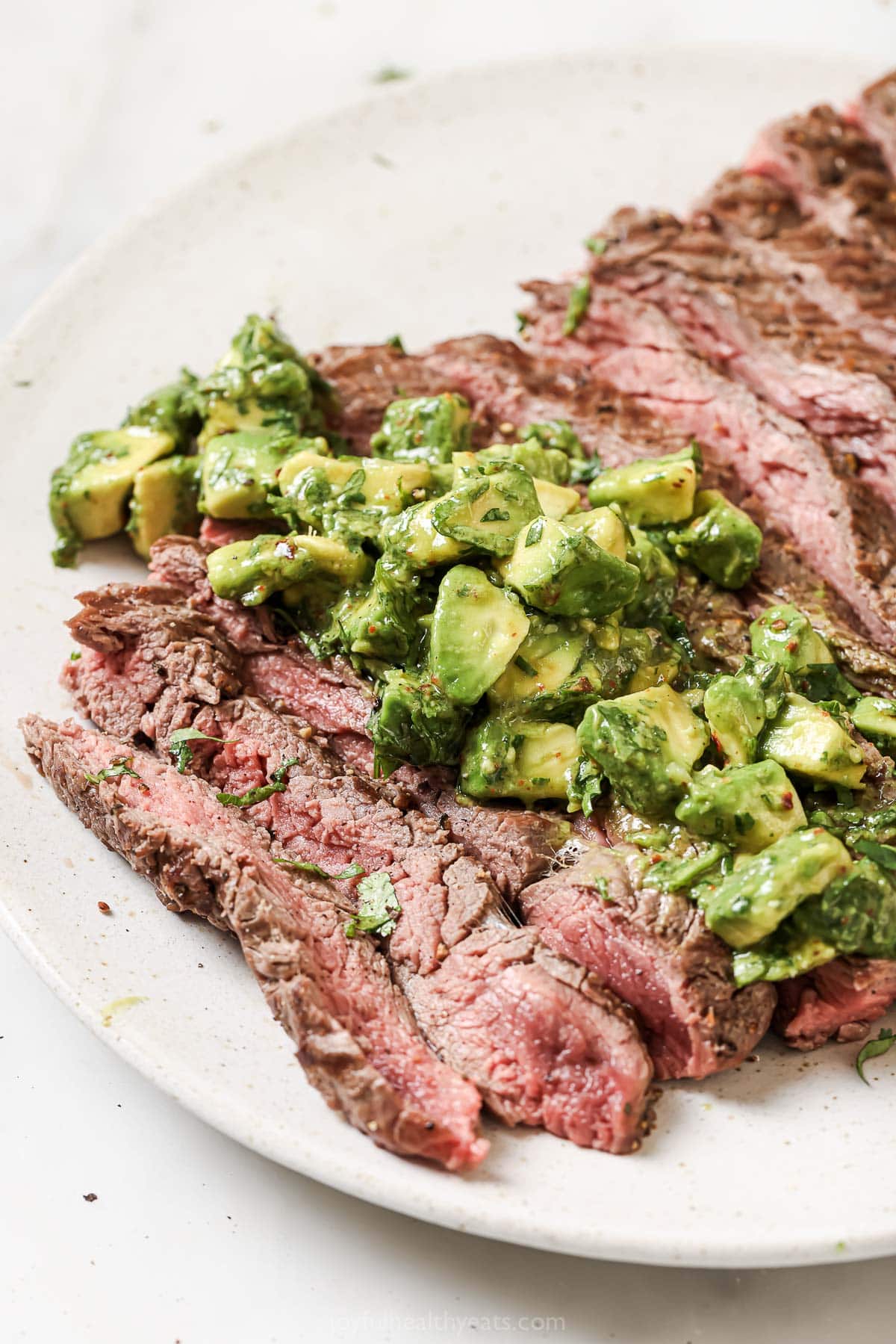This juicy Grilled Flank Steak with Avocado Chimichurri is an easy recipe that’s full of flavor. It’s ready in less than 20 minutes! Grilled flank steak on plate with avocado chimichurri on top