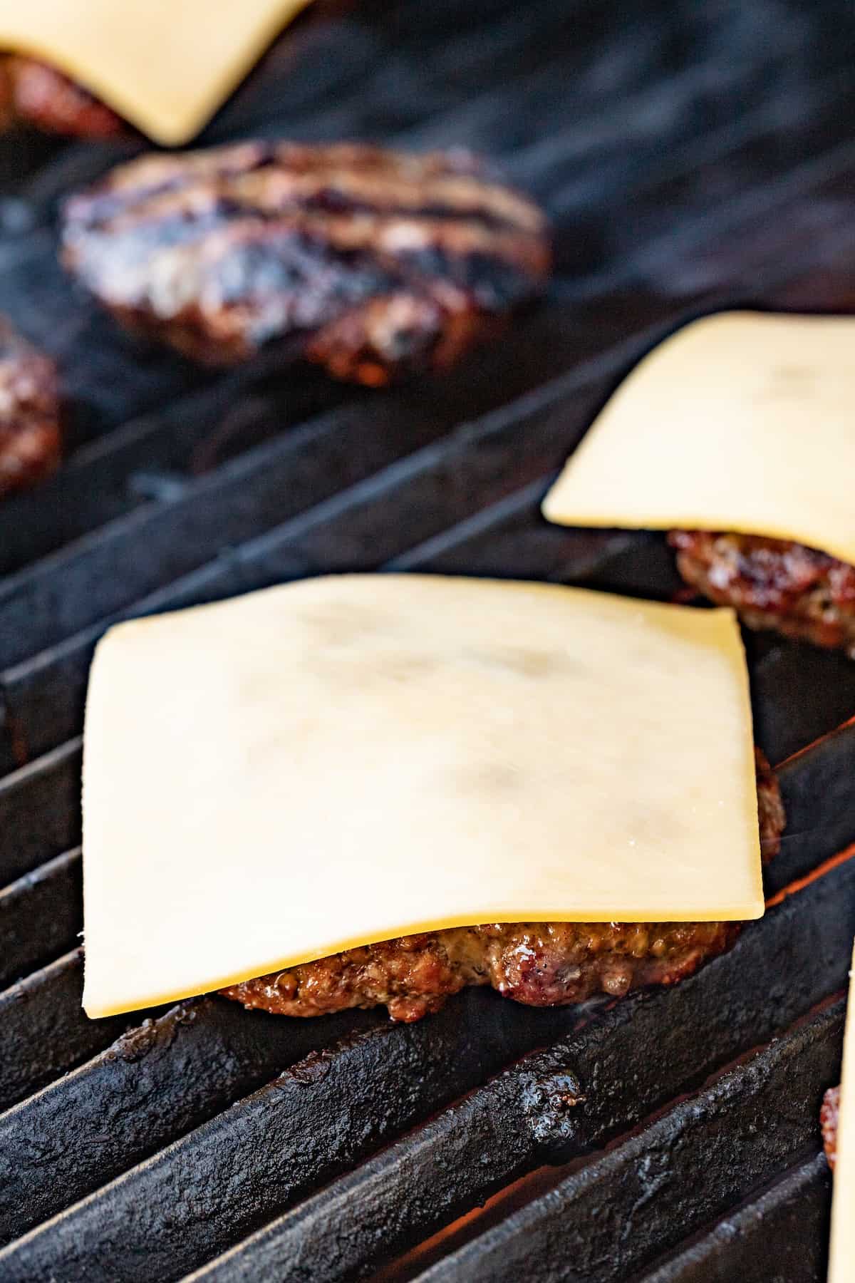 This 15-minute Italian cheeseburger is loaded with gouda cheese, sun-dried tomatoes, pesto aioli, and prosciutto for the perfect bite. Placing the cheese on the cooked patties.