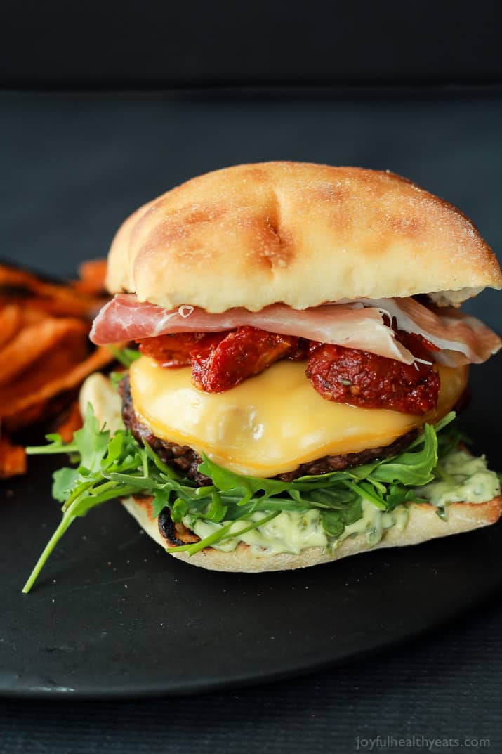 A juicy Italian Cheeseburger served on a toasted ciabatta bun, topped with smoked gouda cheese, spicy arugula, sun dried tomatoes, salty prosciutto, and basil pesto aioli! Done in 15 minutes this Burger is sure to be your new favorite this summer! | joyfulhealthyeats.com #recipes #grill #easy