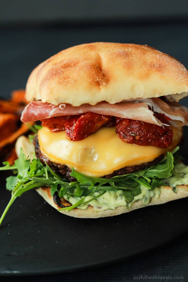 A juicy Italian Cheeseburger served on a toasted ciabatta bun, topped with smoked gouda cheese, spicy arugula, sun dried tomatoes, salty prosciutto, and basil pesto aioli! Done in 15 minutes this Burger is sure to be your new favorite this summer! | joyfulhealthyeats.com #recipes #grill #easy