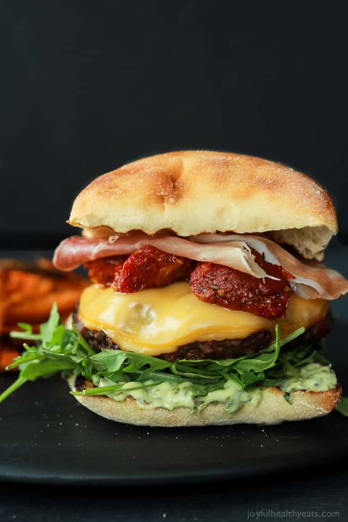 A juicy Italian Cheeseburger served on a toasted ciabatta bun, topped with smoked gouda cheese, spicy arugula, sun dried tomatoes, salty prosciutto, and basil pesto aioli! Done in 15 minutes this Burger is sure to be your new favorite this summer! | joyfulhealthyeats.com #recipes #grill #easy