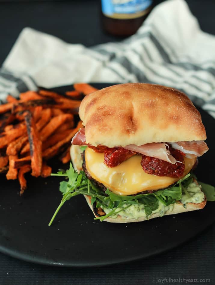 A juicy Italian Cheeseburger served on a toasted ciabatta bun, topped with smoked gouda cheese, spicy arugula, sun dried tomatoes, salty prosciutto, and basil pesto aioli! Done in 15 minutes this Burger is sure to be your new favorite this summer! | joyfulhealthyeats.com #recipes #grill #easy
