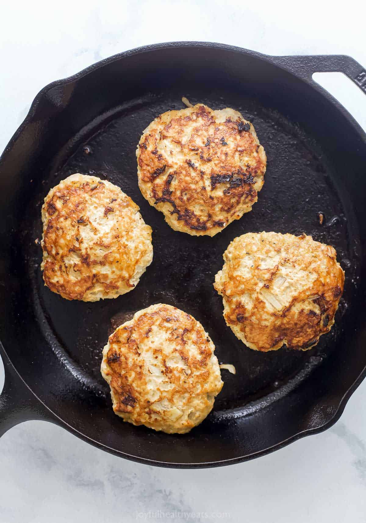 These BBQ Chicken Burgers are easy to make and perfect for summer parties and weeknight dinners. So flavorful and juicy! Overhead view of chicken burger patties cooking in cast iron skillet