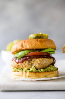 Chicken burger on brioche bun with lettuce, tomato, BBQ sauce, and mashed avocado