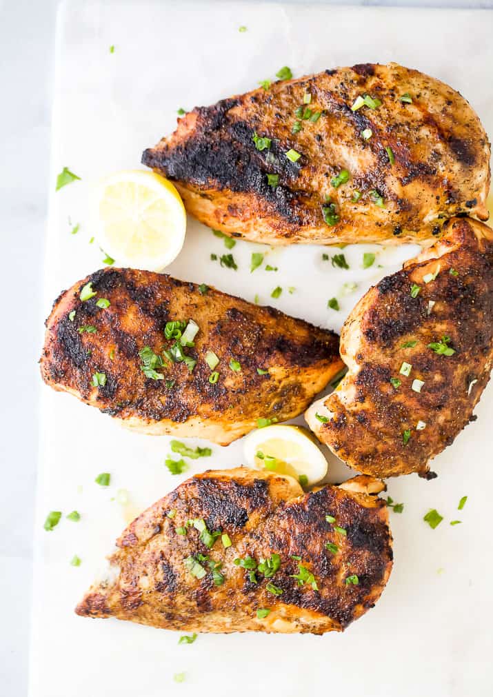cooked grilled chicken breasts on a white plate with lemon slices