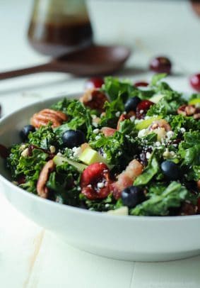 A Summer Kale Salad Recipe that will blow your mind! Filled with fresh cherries and blueberries for some sweet then countered with salty bacon and feta. Perfect for a backyard bbq party this summer, its even Red White and Blue! | joyfulhealthyeats.com #recipe