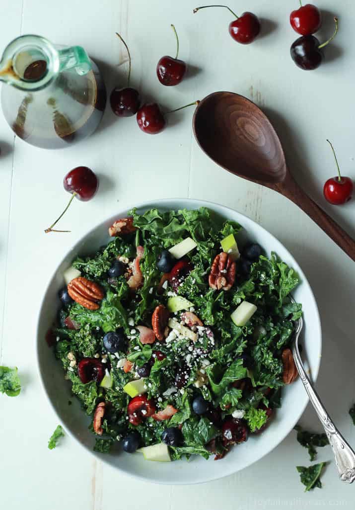 Top view of Summer Kale Salad next to balsamic vinaigrette and fresh cherries