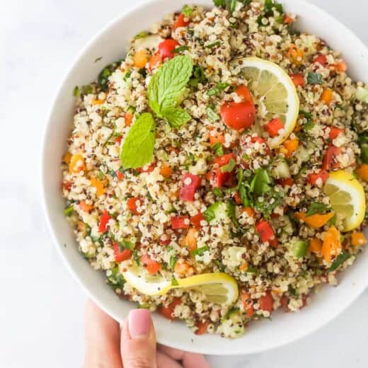 20 minute quinoa tabbouleh salad in a bowl with a hand holding the bowl