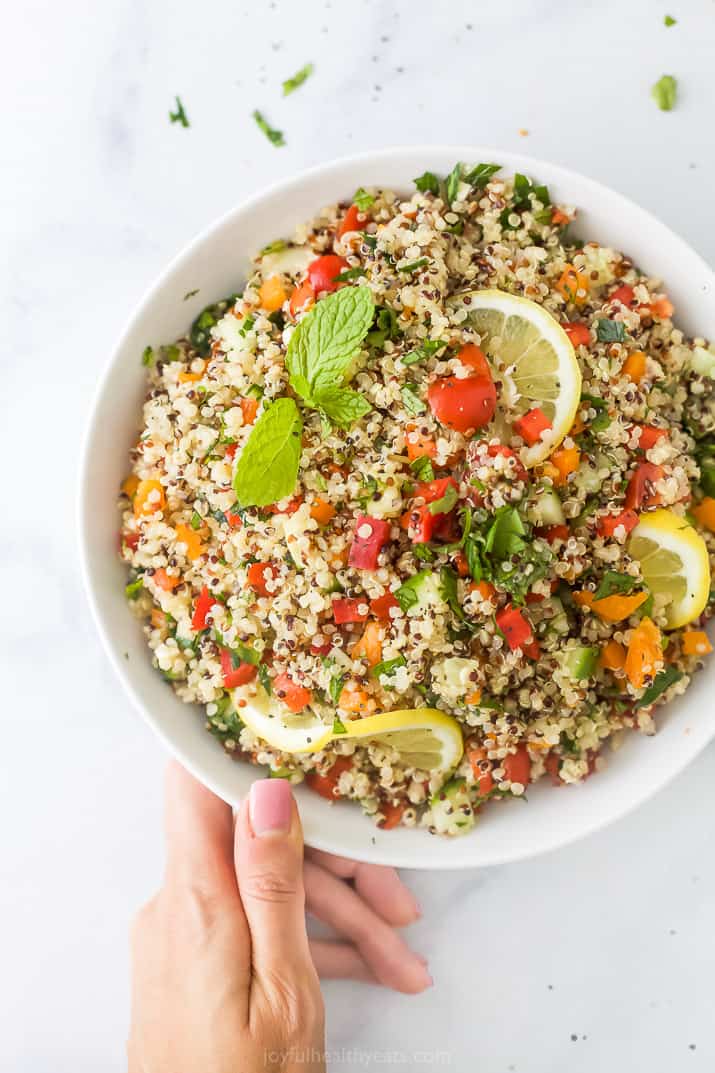 20 minute quinoa tabbouleh salad in a bowl with a hand holding the bowl
