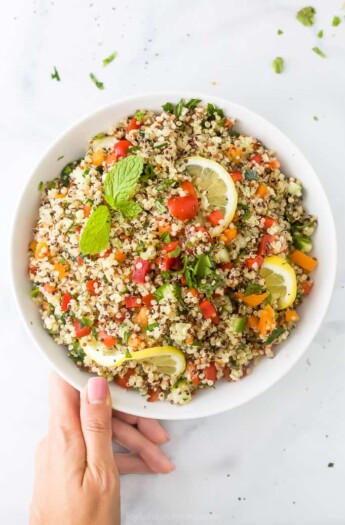 20 minute quinoa tabbouleh salad in a bowl with a hand on the bowl