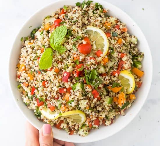 20 minute quinoa tabbouleh salad in a bowl with a hand on the bowl