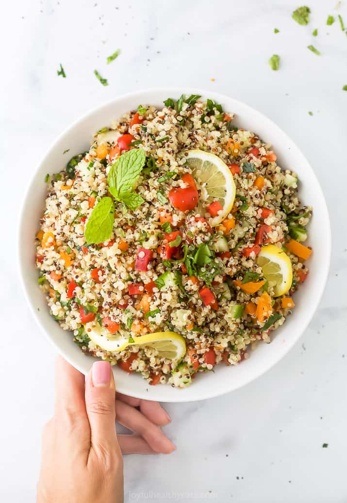 20 minute quinoa tabbouleh salad in a bowl with a hand on the bowl