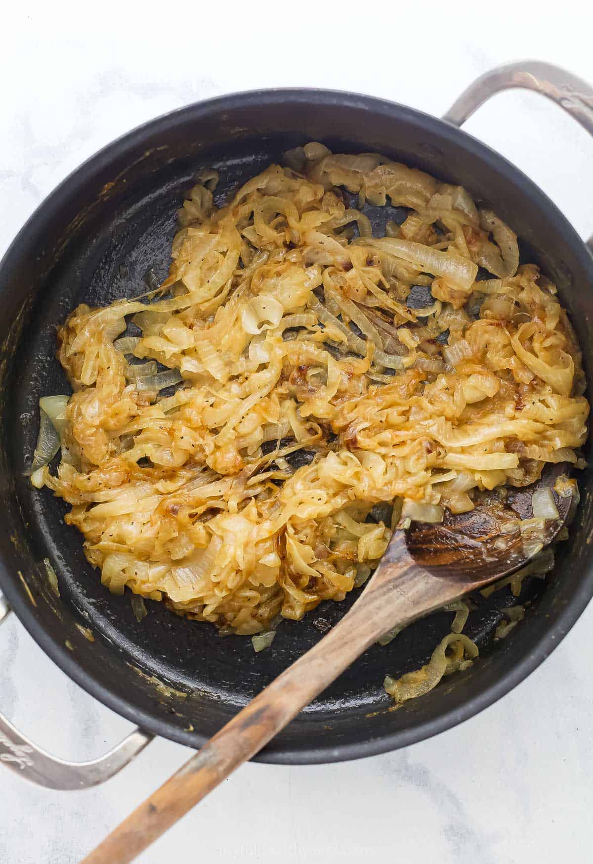 Skillet of caramelized onions with wooden spoon.